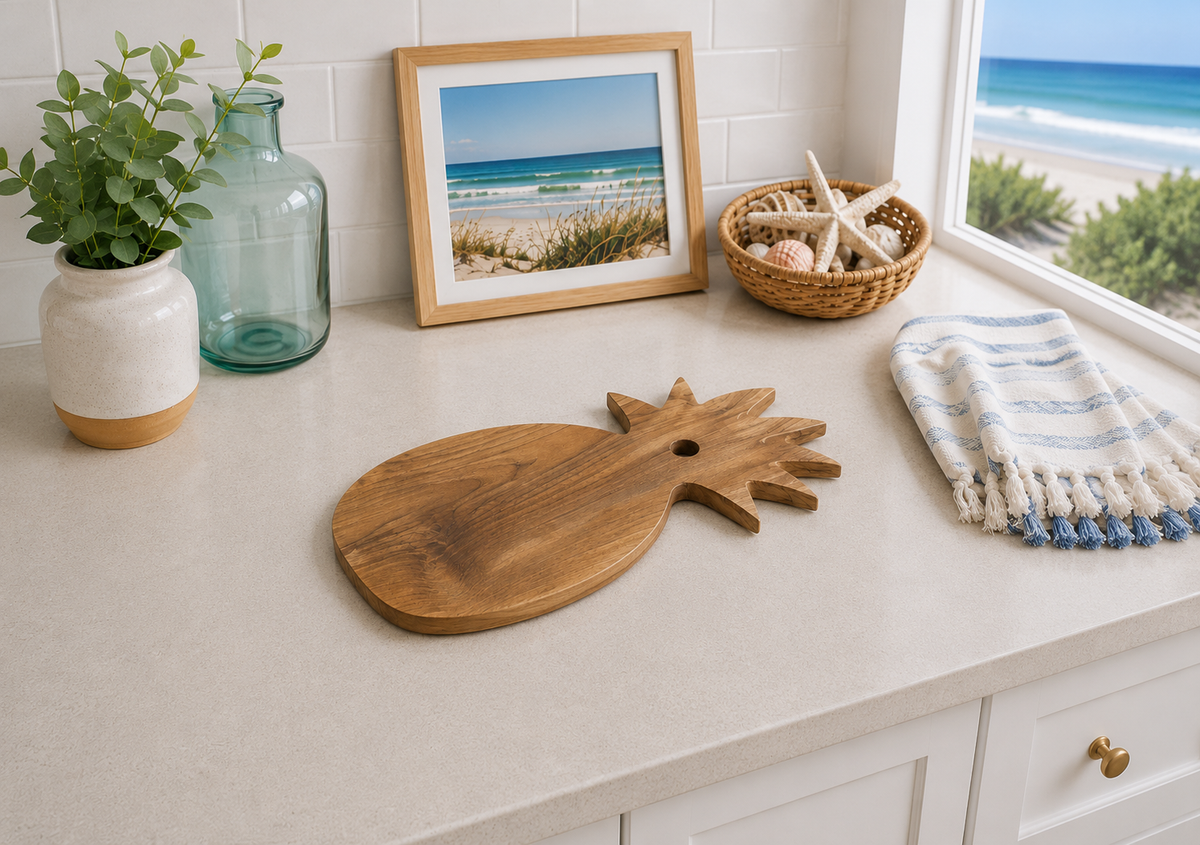 Wooden pineapple-shaped cutting board on a kitchen counter with decorative items and a view of the ocean.